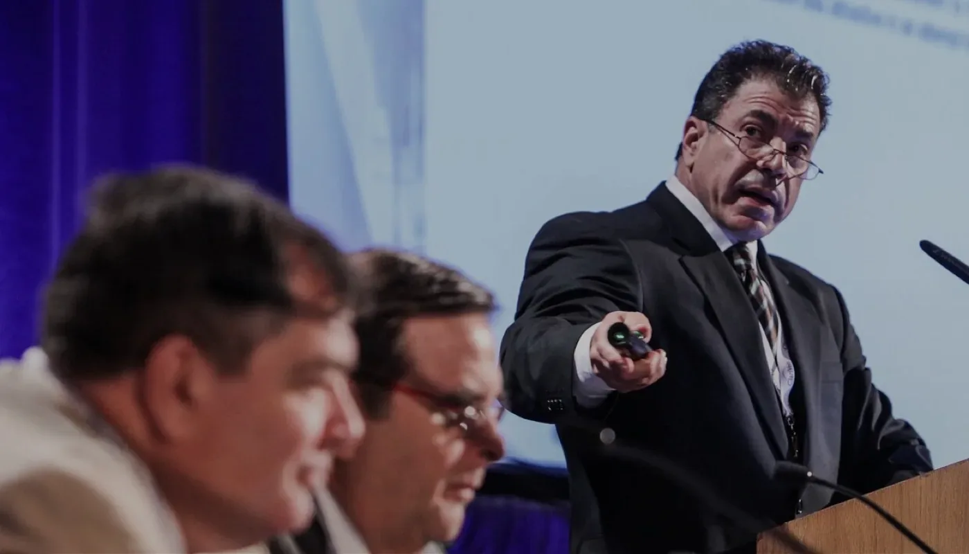 Dr. Jose Almeida presenting from the podium at a vein conference, gesturing toward the panel