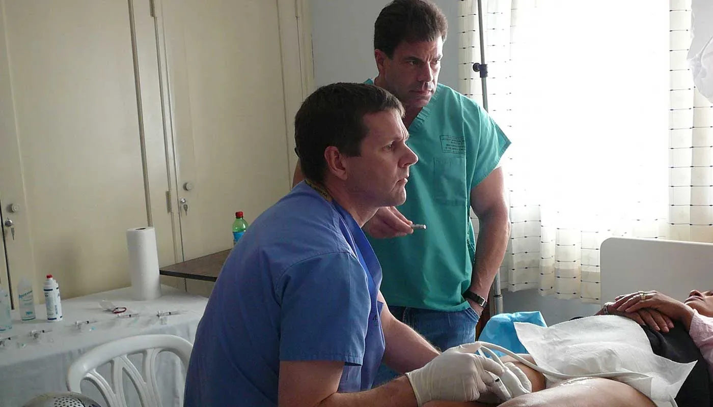 Dr. Jose Almeida teaching ultrasound-guided vein care at a patient's bedside as a trainee observes